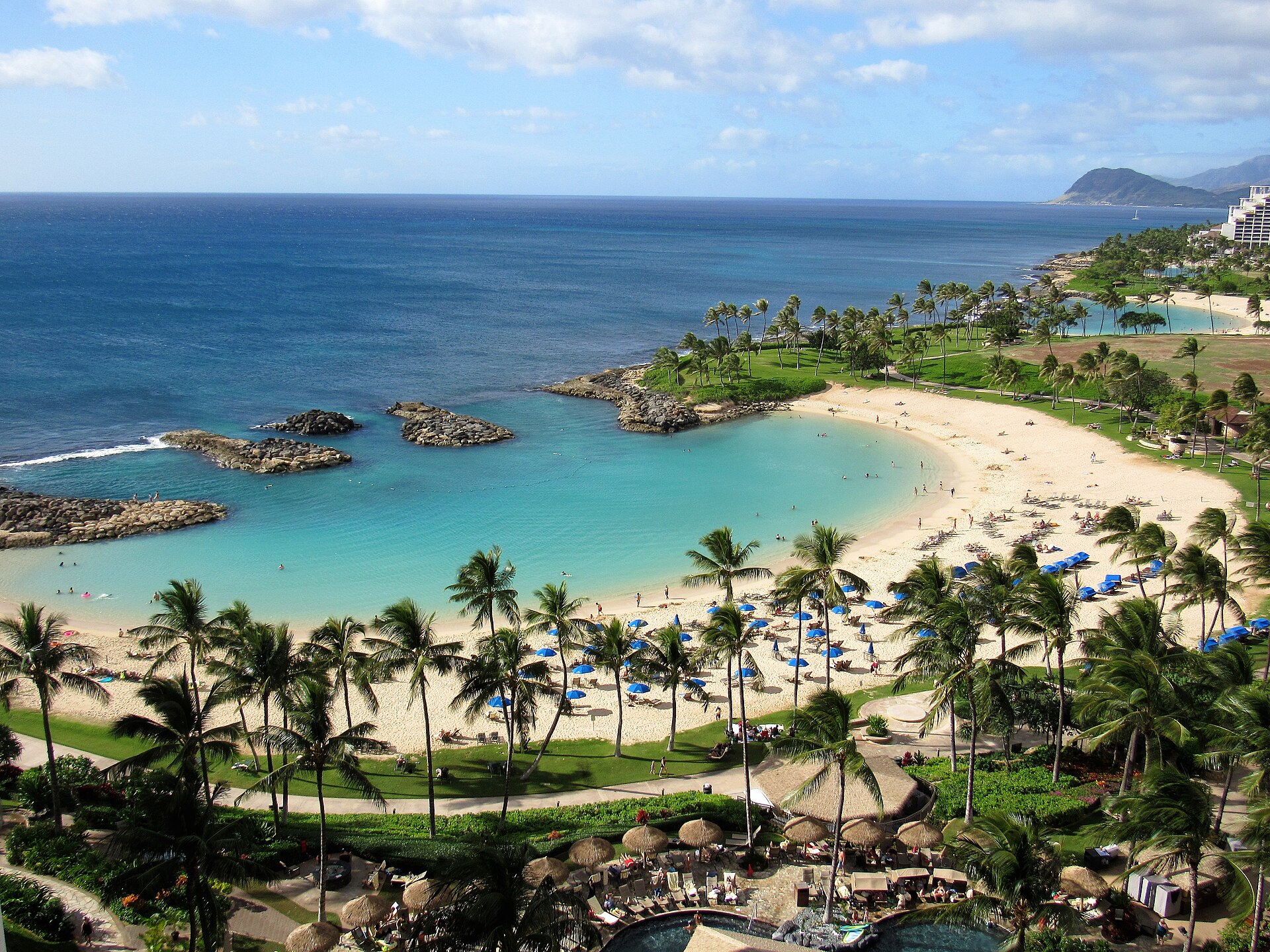 A calm, sheltered turquoise lagoon with a curved sand beach and palm trees at Ko Olina on Oahu, Hawaii