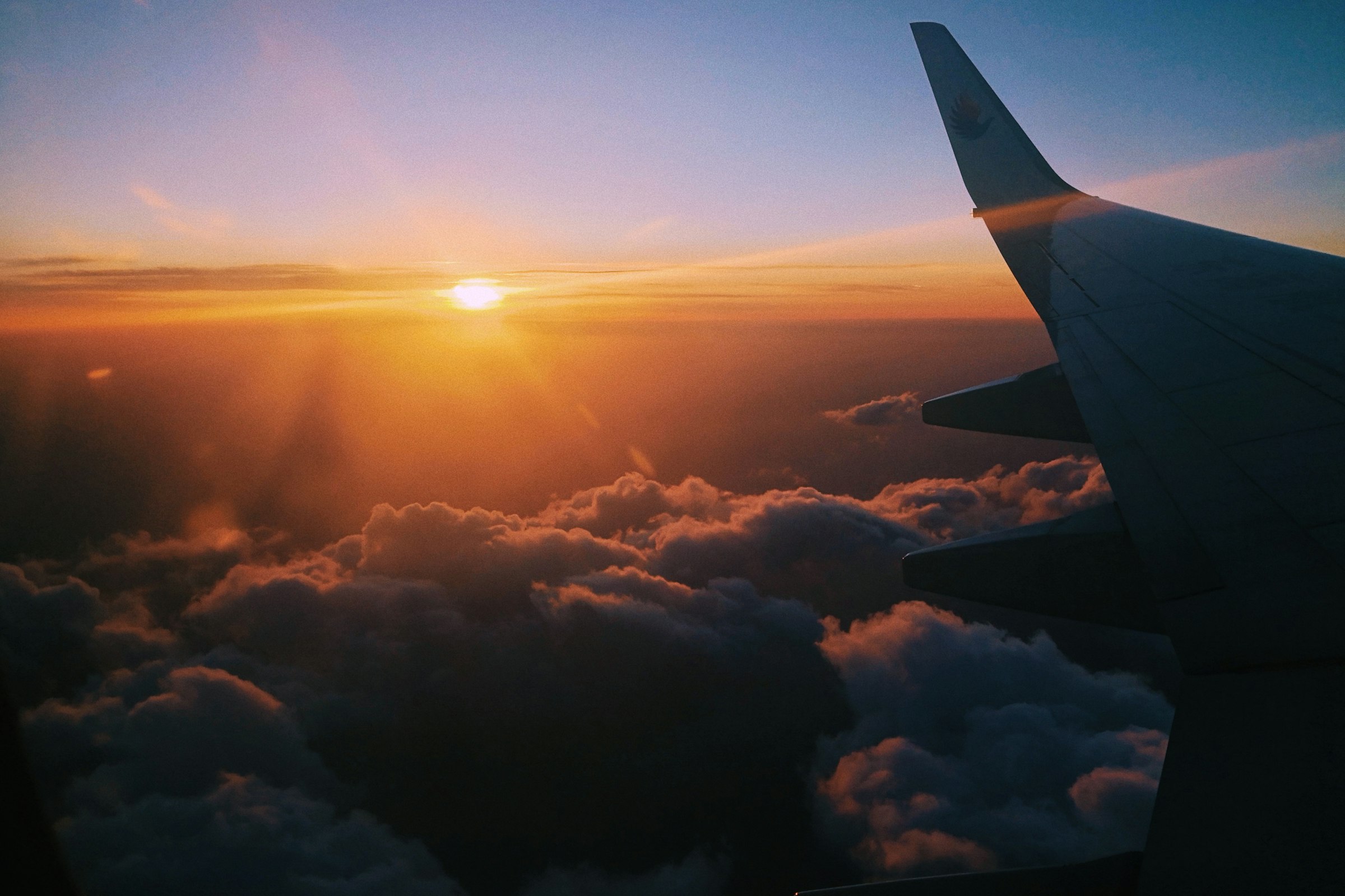 Airplane wing over a sea of clouds at golden hour, the sun low on the horizon